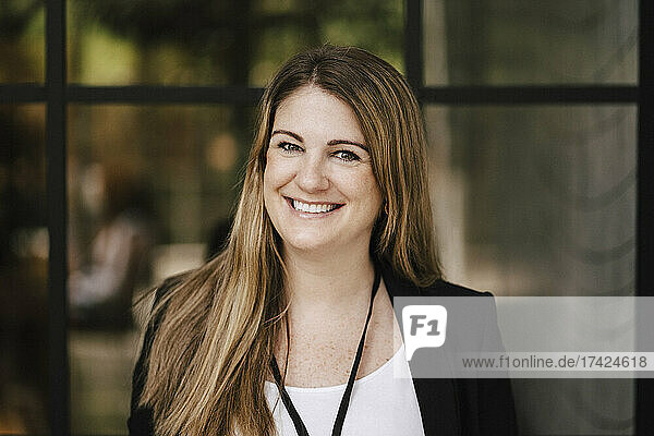 Porträt einer glücklichen Geschäftsfrau  die vor einer Glaswand im Kongresszentrum steht