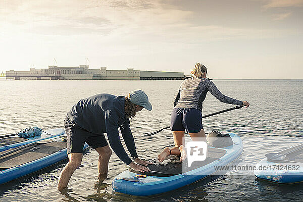 Frau lernt Paddleboarding von männlichem Lehrer im Meer bei Sonnenuntergang