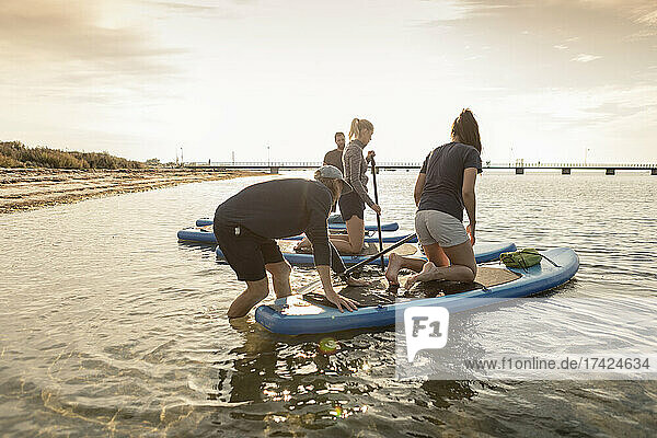 Man and women learning to paddleboard from male instructor in sea at beach