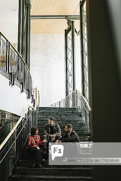 Männliche und weibliche Fachleute in voller Länge  die auf einer Treppe sitzend während einer Networking-Veranstaltung auf einem Kongress diskutieren
