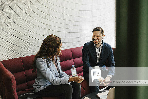 Fröhliche männliche und weibliche Unternehmer diskutieren auf dem Sofa sitzend während einer Netzwerkveranstaltung