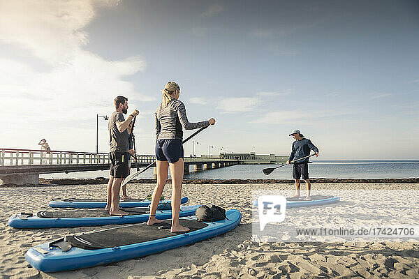 Männlicher Lehrer unterrichtet Mann und Frau am Strand im Paddleboarding