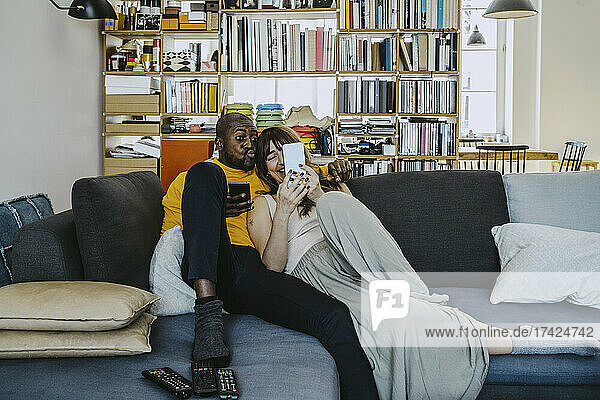 Frau  die ein Selfie mit ihrem Freund macht  während sie zu Hause auf dem Sofa im Wohnzimmer sitzt