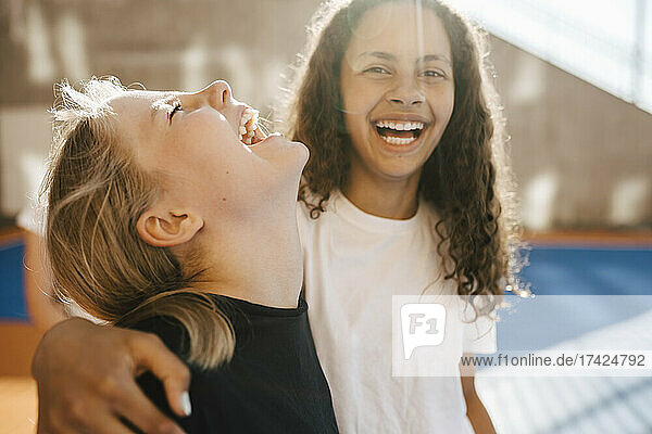 Cheerful female friends laughing at basketball court on sunny day