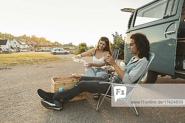 Young couple having food outside camping van in evening