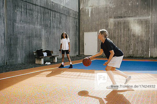 Vorpubertäres Mädchen dribbelt Basketball  während sie mit einer Freundin im Hof spielt