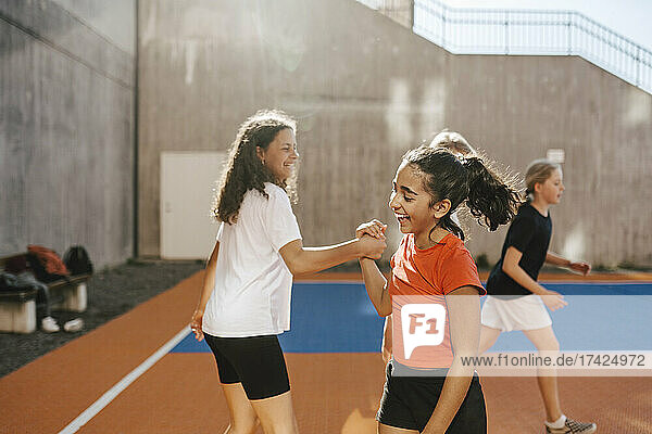 Glückliche Freundinnen halten sich die Hände  während sie auf dem Basketballplatz spielen
