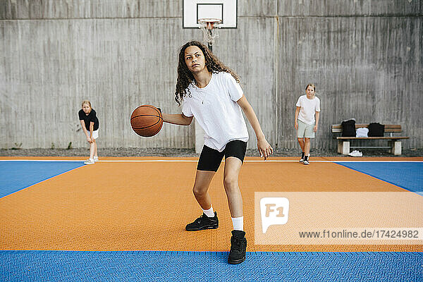 Vorpubertäres Mädchen  das wegschaut  während es auf dem Platz Basketball übt