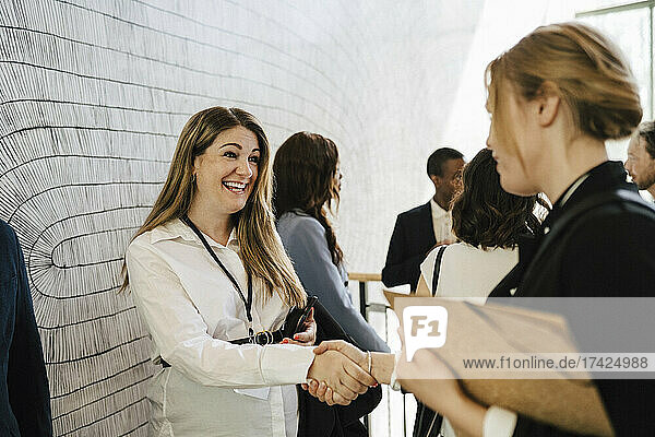 Glückliche schwangere Unternehmerin  die eine Geschäftsfrau beim Händeschütteln während einer Netzwerkveranstaltung begrüßt