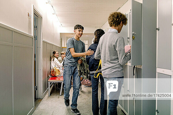 Teenage boys and girls near locker in corridor at school building