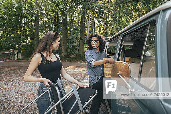 Male and female friends removing chair and crate from camping van