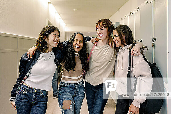 Smiling female friends standing together in corridor of school