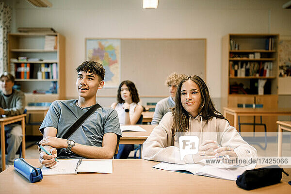 Smiling junior high students with book and pen studying in illuminated classroom