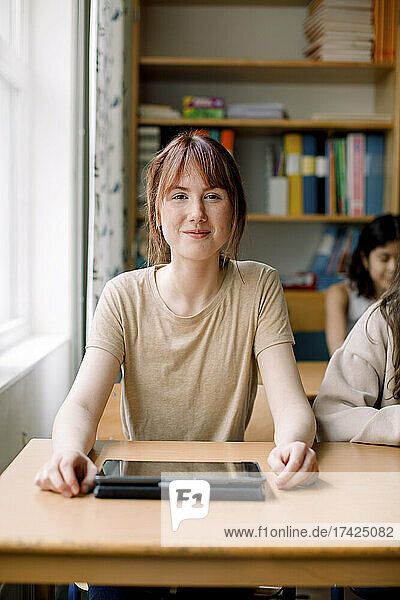Lächelndes Teenager-Mädchen mit digitalem Tablet auf dem Schreibtisch im Klassenzimmer