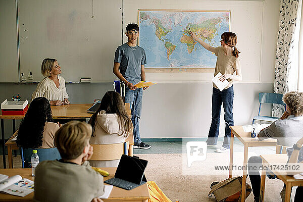 Teenager und Mädchen erklären über Weltkarte im Klassenzimmer