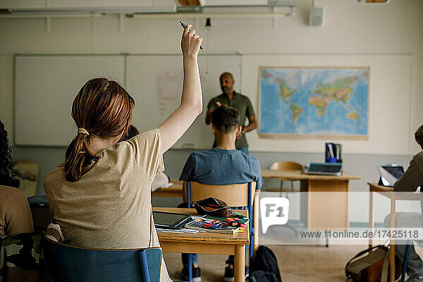 Jugendlicher Schüler hebt die Hand beim Lernen im Klassenzimmer der High School