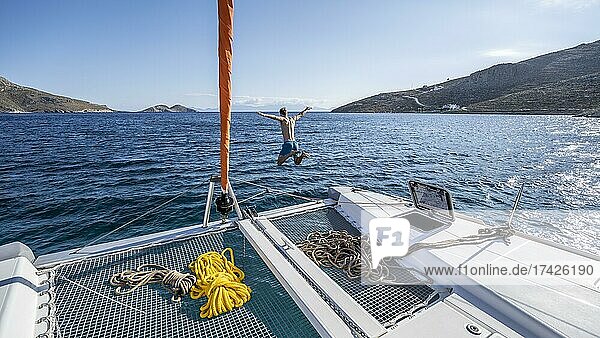 Young man jumps into the water  ropes on a sailing catamaran  sailing trip  Tilos  Dodecanese  Greece  Europe