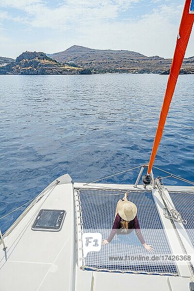 Junge Frau mit Hut sitzt im Netz eines Segel-Katamaran  Segeltörn  Rhodos  Dodekanes  Griechenland  Europa