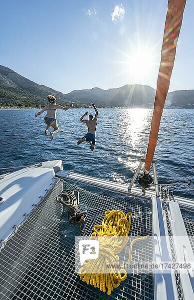 Young woman and young man jumping into the water  ropes on a sailing catamaran  Sun Star  sailing trip  Tilos  Dodecanese  Greece  Europe