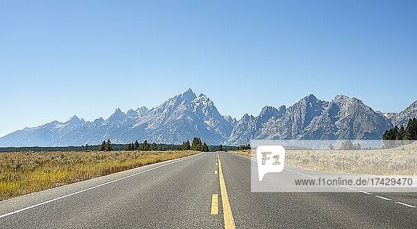 Country road through autumn landscape  rugged mountain peaks behind  Grand Teton and The Jaw  Teton Range mountain range  Grand Teton National Park  Wyoming  USA  North America