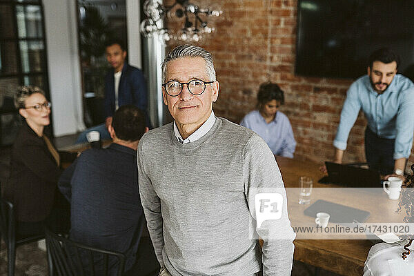 Portrait of mature male entrepreneur standing while colleagues discussing in background