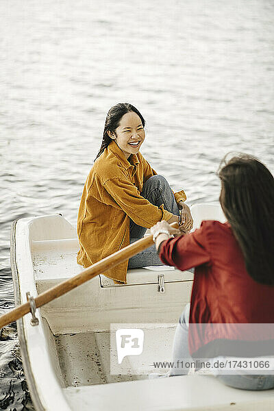 Glückliche junge Frau  die auf eine Freundin blickt  die ein Boot rudert