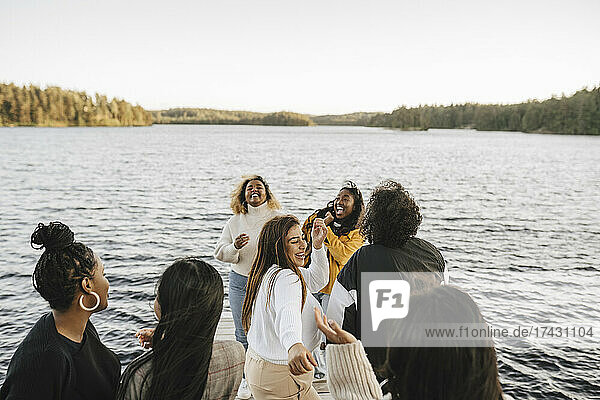 Happy female friends dancing at lakeshore against clear sky