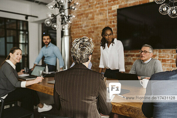 Reife Geschäftsfrau sitzt am Konferenztisch und bespricht einen Plan mit ihrem Team im Sitzungssaal