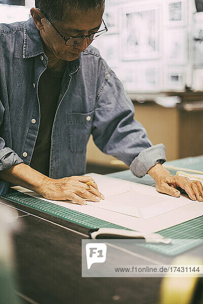 Ein älterer Handwerker prüft Papier bei der Arbeit in der Werkstatt