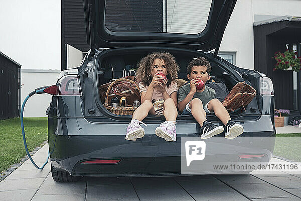Bruder und Schwester essen Äpfel  während sie im Kofferraum eines Autos sitzen