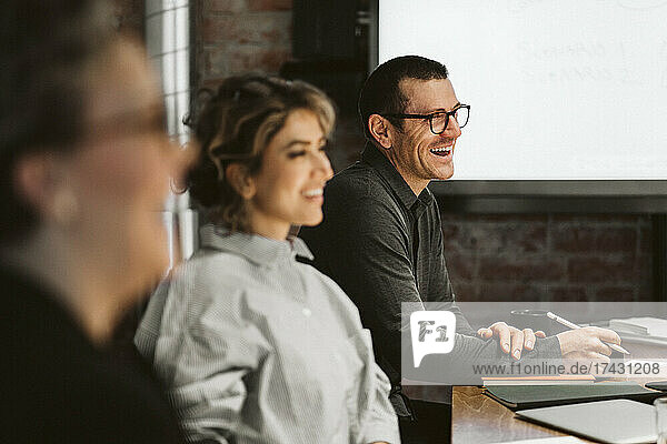 Reifer männlicher Berufstätiger  der lachend neben weiblichen Kollegen im Sitzungssaal sitzt