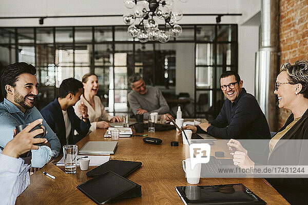 Cheerful business professionals laughing while sitting at conference table in board room