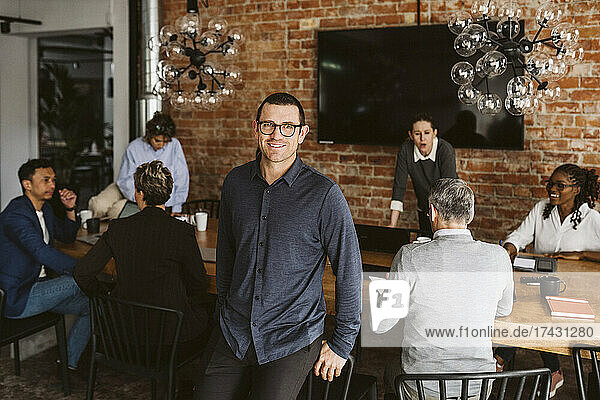 Portrait of smiling businessman standing while colleagues discussing in background