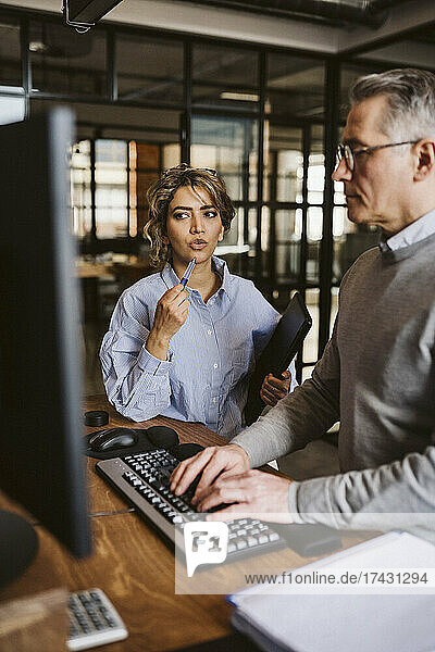 Female professional discussing with businessman using computer at desk