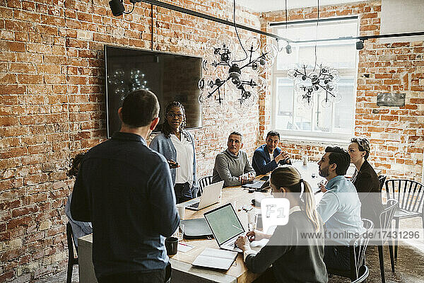 Businesswoman and businessman discussing strategy with colleagues during meeting in board room