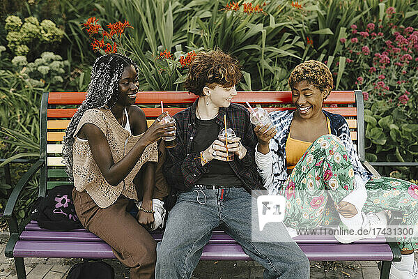 Glückliche LGBTQIA-Freunde genießen ein Getränk auf einer Bank im Park
