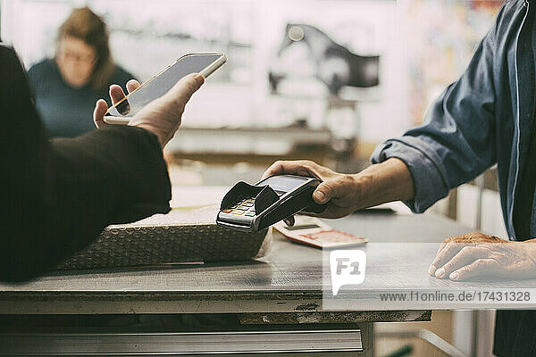Abgeschnittene Hand einer Kundin beim kontaktlosen Bezahlen in einem Einzelhandelsgeschäft