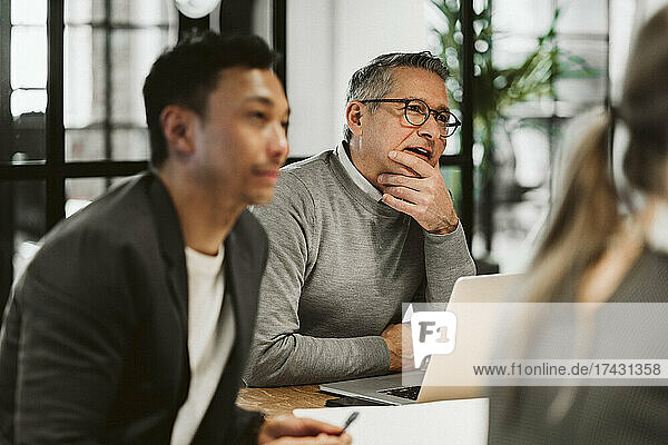 Reifer Geschäftsmann sitzt mit Hand am Kinn neben einem männlichen Kollegen im Sitzungssaal
