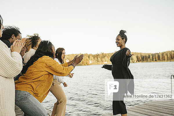 Happy female friends cheering woman dancing on jetty against clear sky