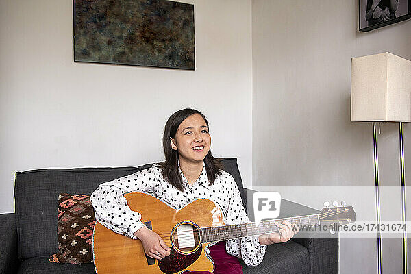 Smiling woman playing acoustic guitar in living room