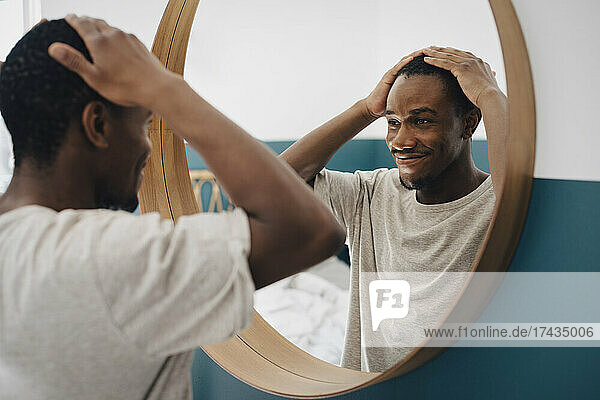 Lächelnder Mann mit Hand im Haar  der zu Hause in den Spiegel schaut