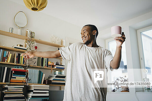 Glücklich Mitte erwachsenen Mann tanzen mit Kaffeetasse im Wohnzimmer zu Hause
