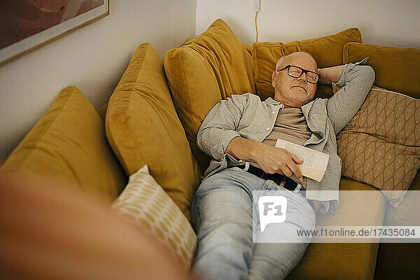Senior man sleeping with book on sofa at home