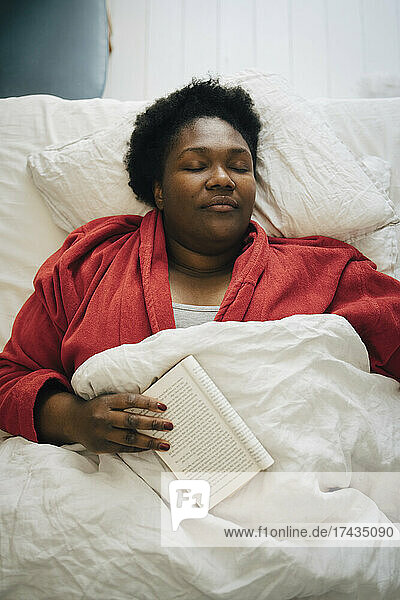 Mid erwachsene Frau in rotem Bademantel schlafen mit Buch auf dem Bett zu Hause