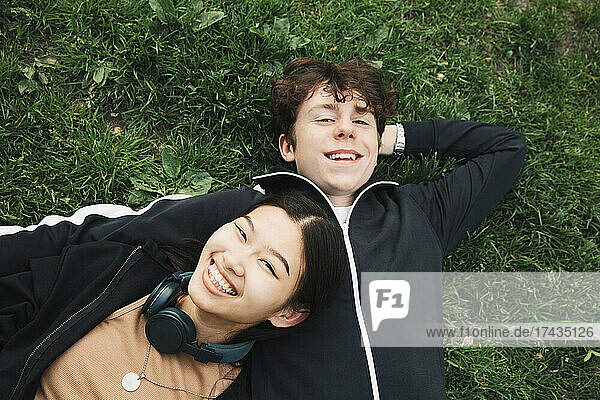 Lächelnde männliche und weibliche Freunde liegen im Gras