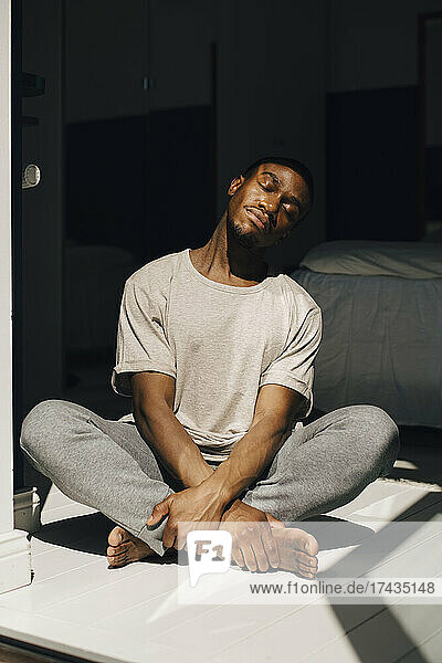 Mittlerer erwachsener Mann meditiert zu Hause im Sonnenlicht