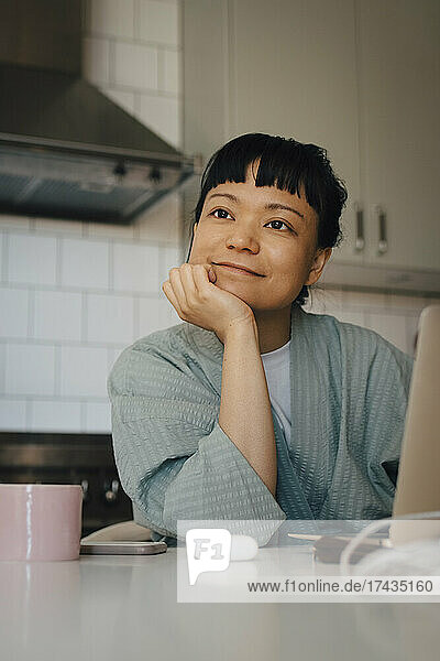 Young woman day dreaming with hand on chin in domestic kitchen