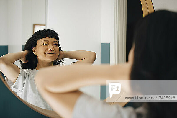 Spiegelung einer lächelnden Frau mit Hand im Haar zu Hause