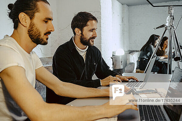 Männliche Hacker arbeiten an Laptops am Schreibtisch in einem kreativen Büro