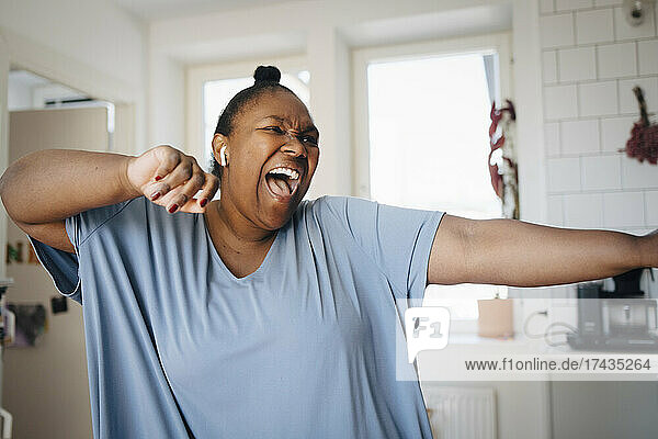 Joyful woman dancing while listening music in kitchen at home